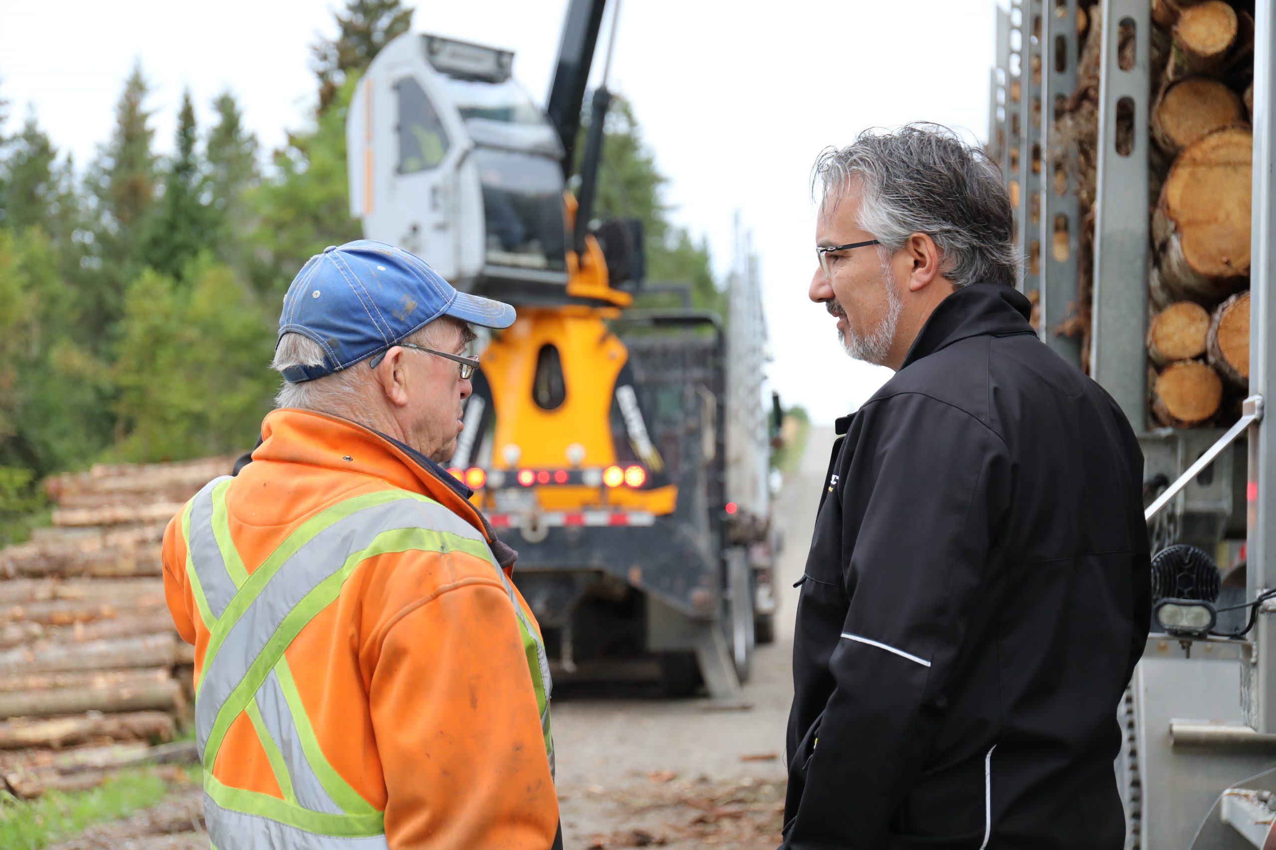 Close-up view of two men talking in front of a Rotobec knuckleboom loader.