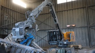 Front view of a loader with a Rotobec trash grapple grabbing waste materials in a warehouse.