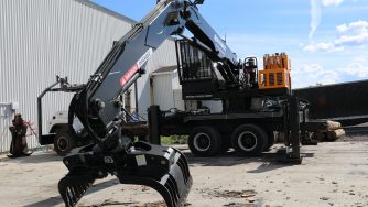 Trash grapple on a loader mounted on a truck in the courtyard of a warehouse.