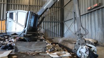 Side view of a loader with a Rotobec trash grapple grabbing waste materials in a warehouse.