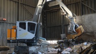 Loader with a Rotobec trash grapple grabbing several wood planks in a warehouse.