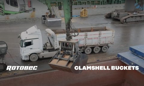 Rotobec clam bucket bringing materials from a container to a truck.