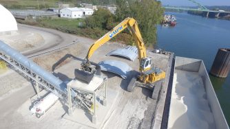 A loader pouring sand with his Rotobec clam bucket into a metal funnel from a container on a ship.
