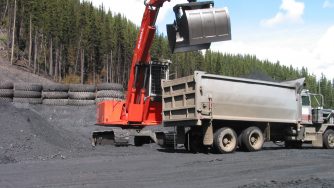 Rotobec clam bucket on a red excavator depositing rocks in a truck.