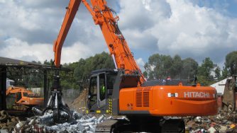 Orange Hitachi loader with a Rotobec orange peel grapple grapping some pieces of metal.