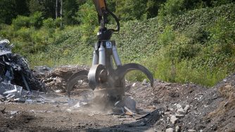 Mag grapple attracting scrap metal with its round magnet leaning to the right.